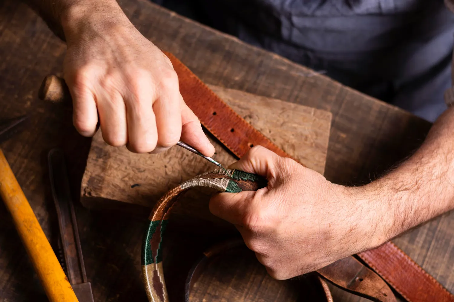 Manos trabajando el canto de un cinturón de cuero en el taller